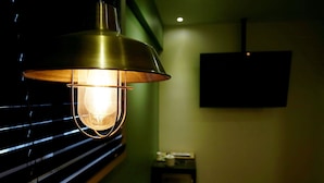 A room with a hanging lamp, a television mounted on the wall, and a small table with items on it. - Achasan Station Wall Hotel (Seoul)