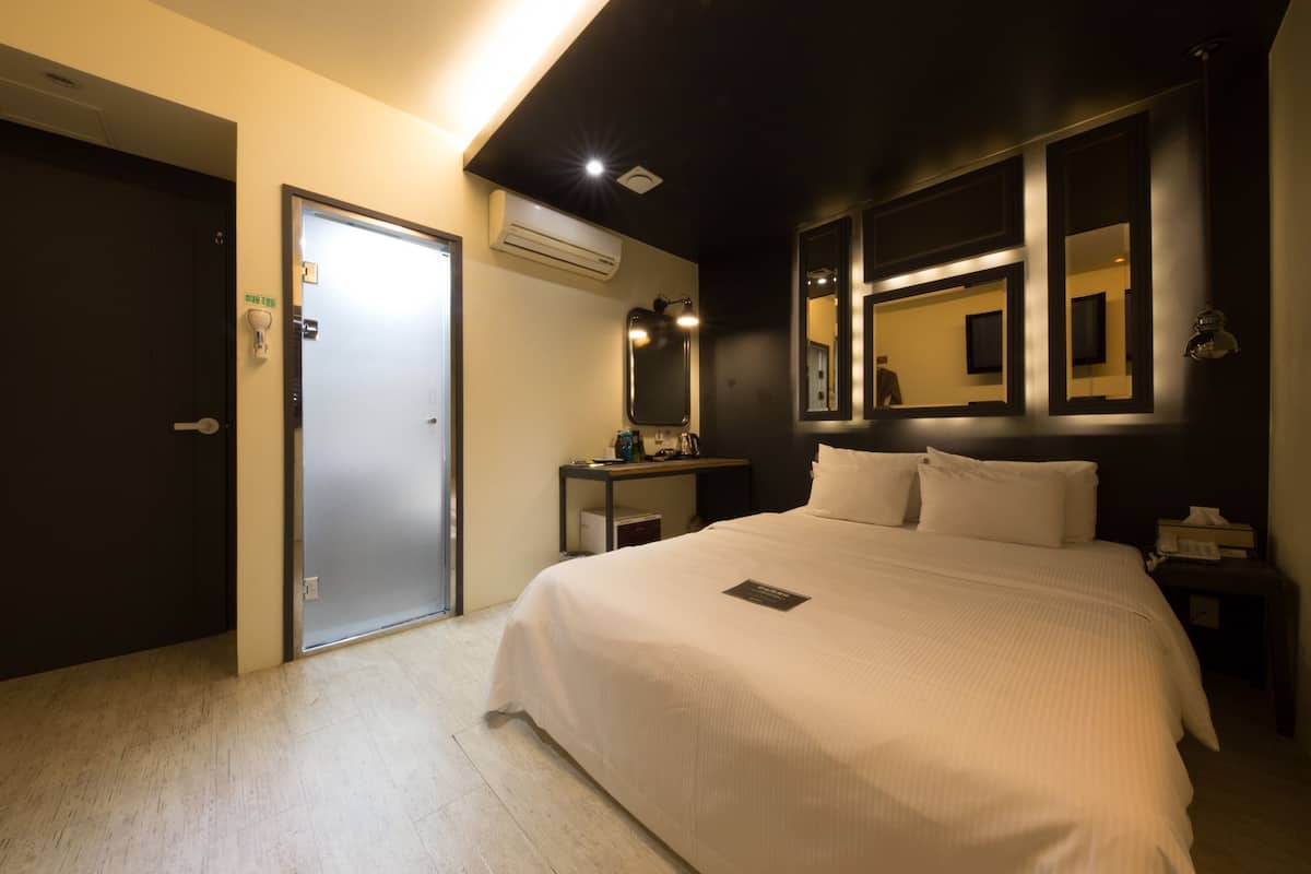 A hotel room with a bed, a nightstand, a mirror, and a door.