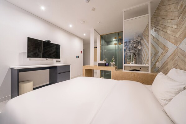 Une chambre d’hôtel moderne dotée d’un grand lit, d’un bureau avec un téléviseur à écran plat, d’une douche en verre et d’un panneau décoratif mural.
