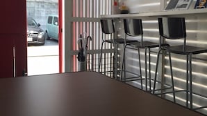 A room with a table, chairs, a bulletin board, and a view of parked cars outside. - Guest House Naraya - Hostel (Fukuoka)