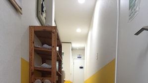 A hotel hallway with a wooden storage unit, striped hats, a welcome mat, and a checkered floor. - Guest House Naraya - Hostel (Fukuoka)