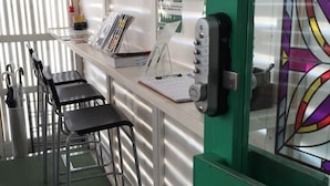 A reception desk with a green counter, a bulletin board, and a clock. There are two chairs and a trash can. - Guest House Naraya - Hostel (Fukuoka)