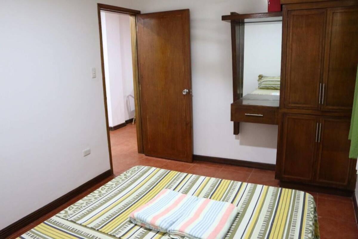 Une chambre à coucher comprenant un lit, une armoire en bois, un miroir et une porte donnant sur une autre pièce.