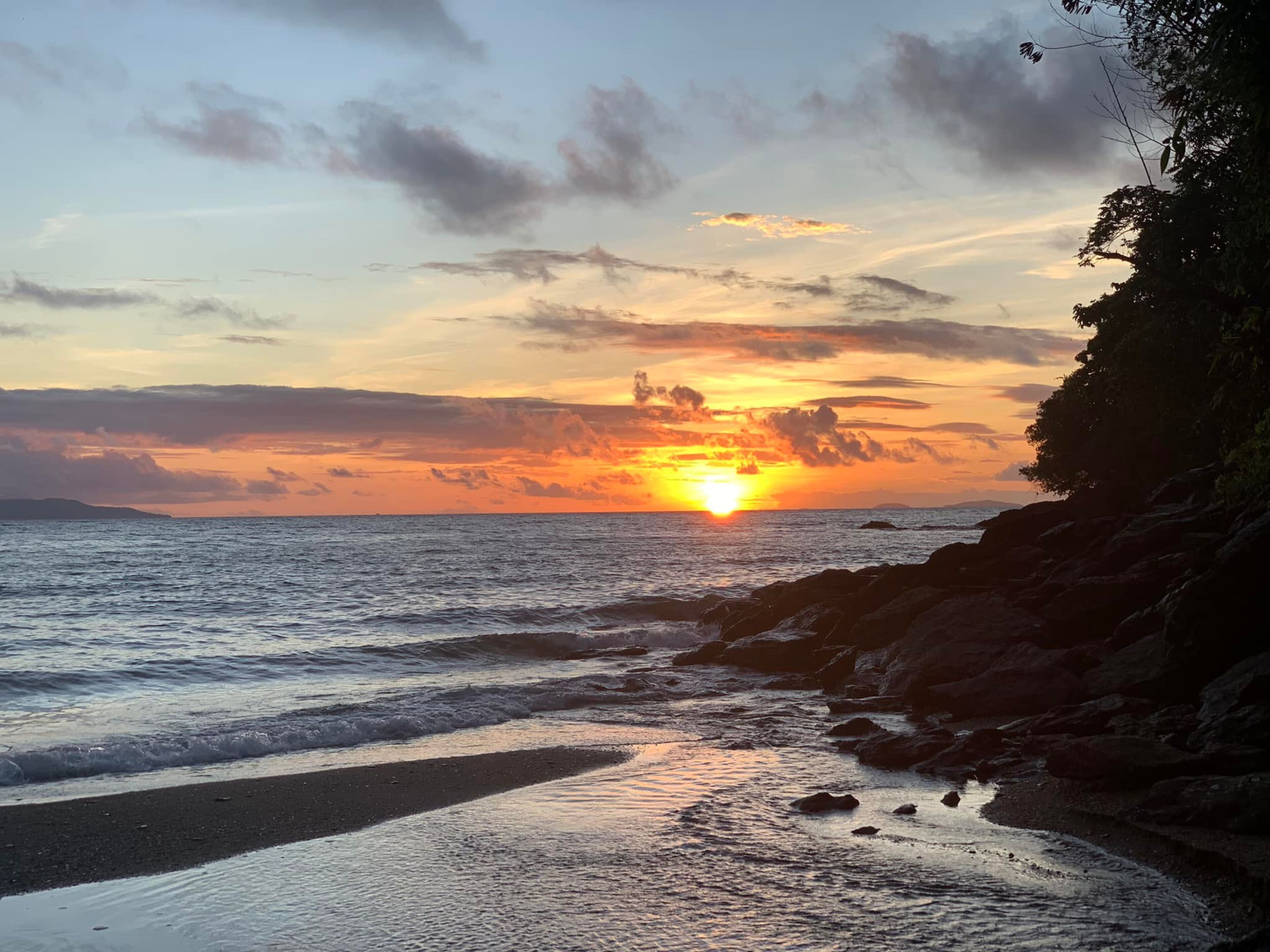 A sunset over a rocky coastline with waves gently lapping at the shore.