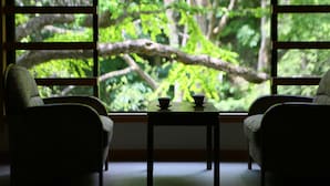Una habitación con dos sillas y una mesa, una ventana con vista a un bosque.