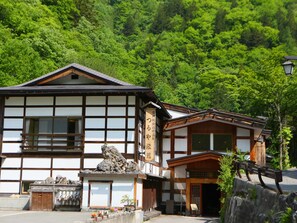 A traditional Japanese building with a wooden exterior and white walls, featuring a stone sculpture and a small garden area with flowers. - Shirahone Onsen Tsuruya Ryokan (Matsumoto)