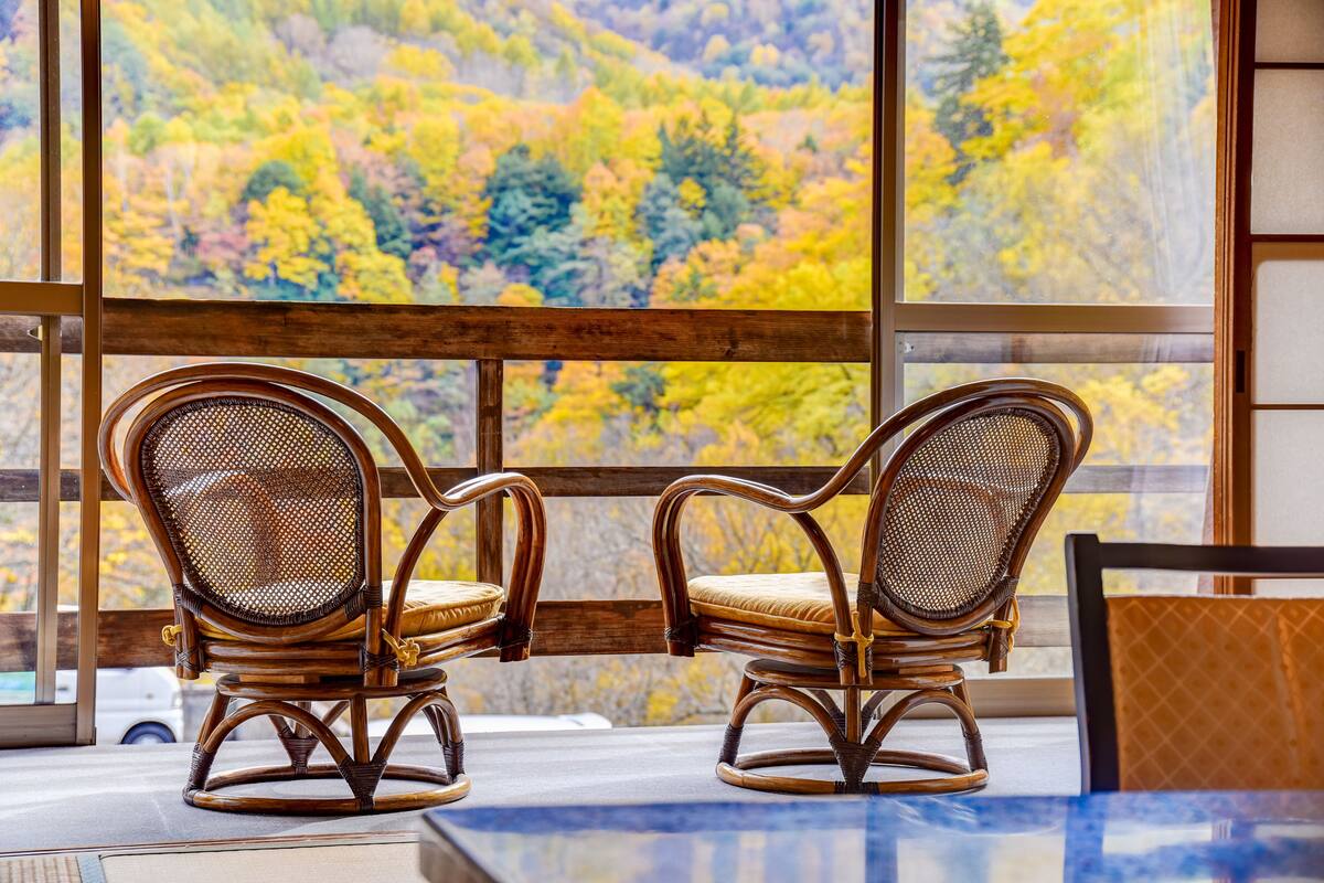 Two wicker chairs with cushioned seats and backs, positioned in front of a window with a view of a forested hillside.