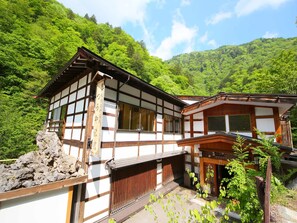 A traditional Japanese-style building with a wooden exterior and white walls, surrounded by lush greenery and hills. - Shirahone Onsen Tsuruya Ryokan (Matsumoto)