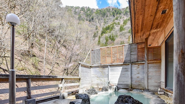 Un área de spa con manantial termal, muelle de madera, sendero de piedra y un edificio de techo inclinado.