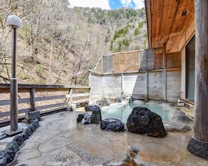 A spa area with a hot spring, wooden deck, stone pathway, and a wooden building with a sloped roof. - Shirahone Onsen Tsuruya Ryokan (Matsumoto)