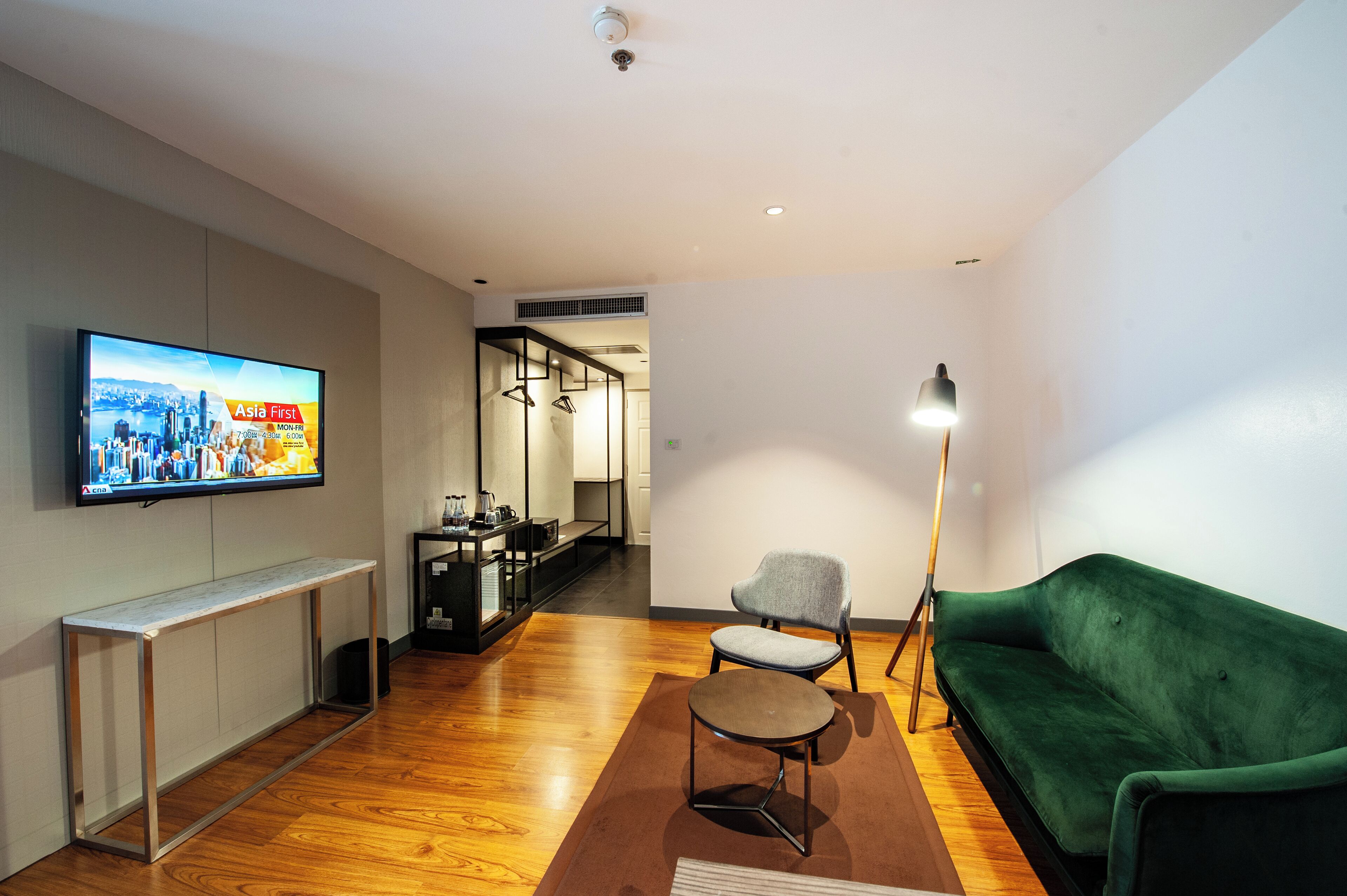 A modern living room with a flat-screen TV, a green sofa, a small round table, and a floor lamp.
