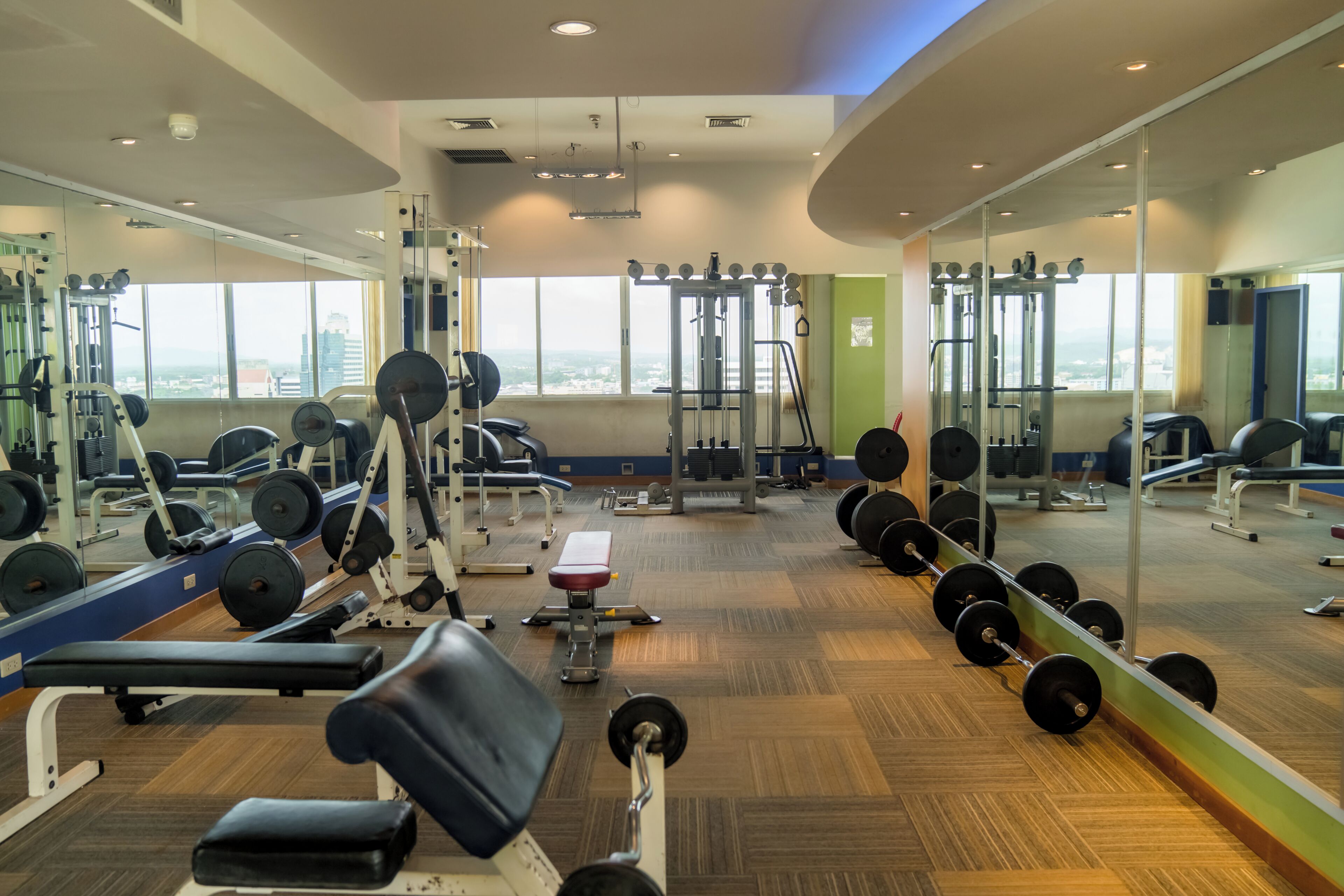 A gym with weightlifting equipment, mirrors, and a bench.