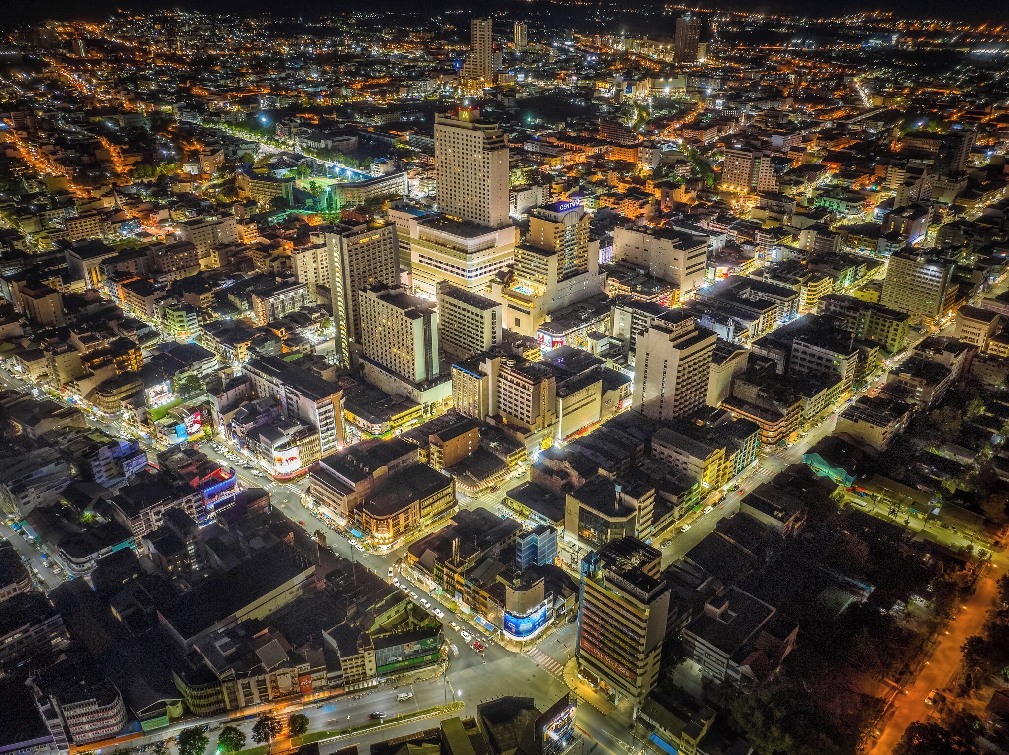 A nighttime aerial view of a densely built urban area with high-rise buildings and illuminated streets.