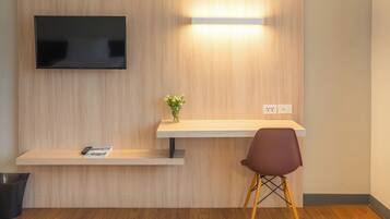 A modern room with a flat-screen TV mounted on the wall, a small desk with a vase of flowers, and a single chair.