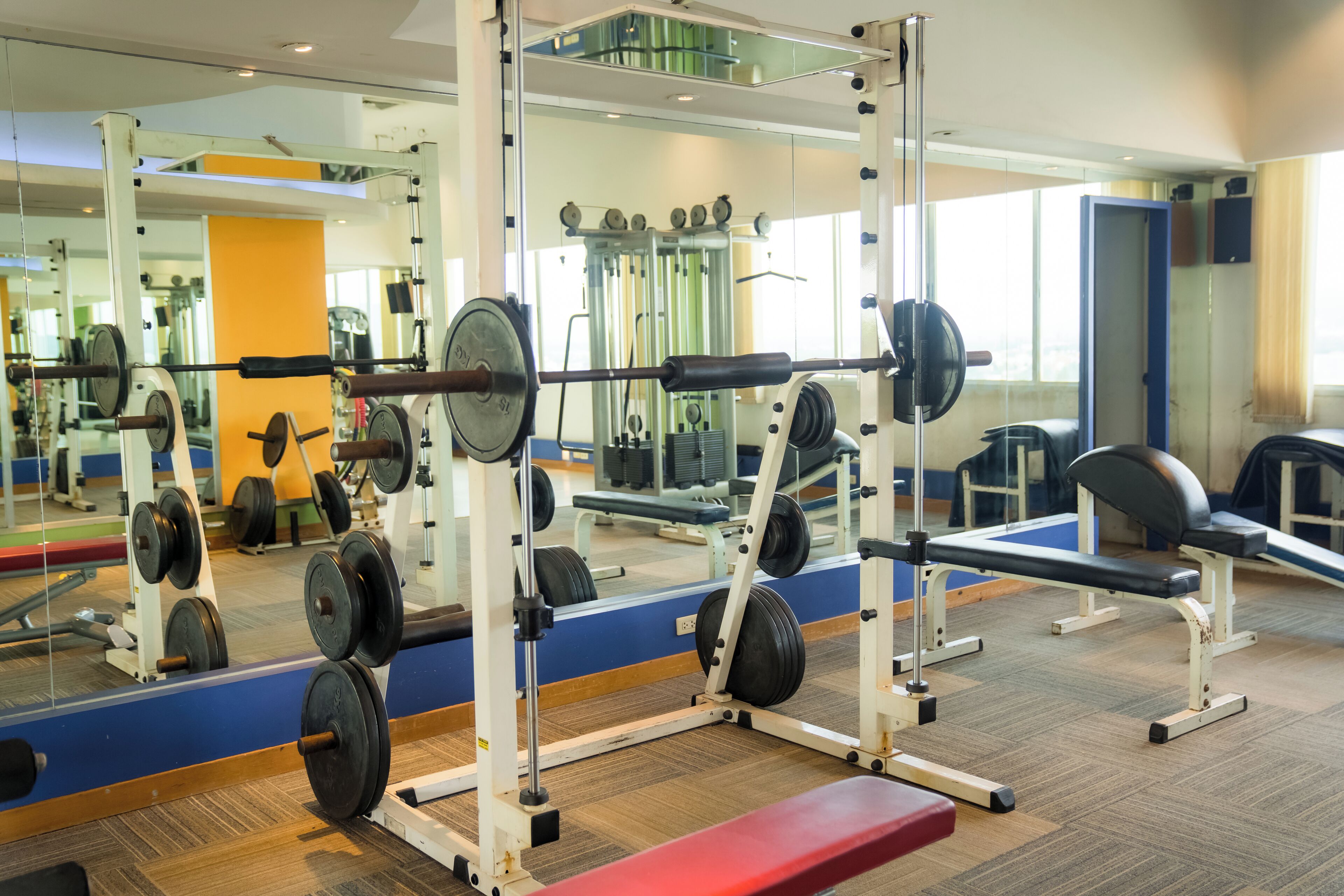 Un gimnasio con equipo de levantamiento de pesas, espejos y bancos de ejercicio.