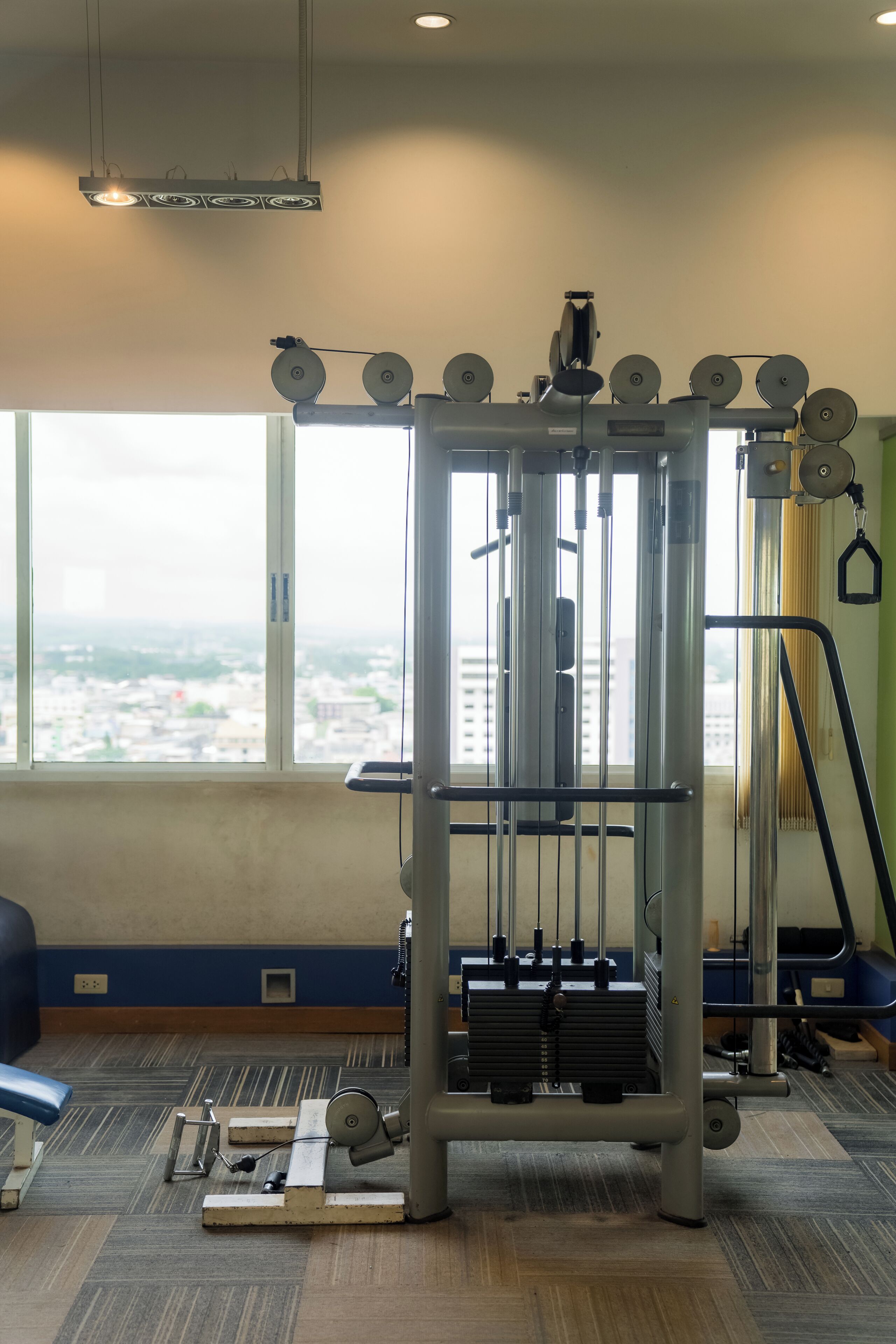 Une salle de sport dotée d’une grande fenêtre, d’un luminaire au plafond et d’appareils d’exercice.
