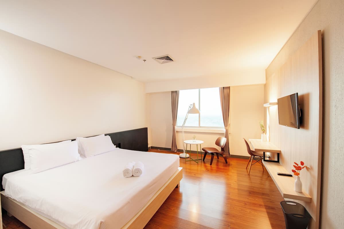 Une chambre d’hôtel avec un grand lit, un bureau, une chaise, une télévision et une fenêtre avec des rideaux.