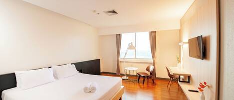 A hotel room with a large bed, a desk, a chair, a TV, and a window with curtains.