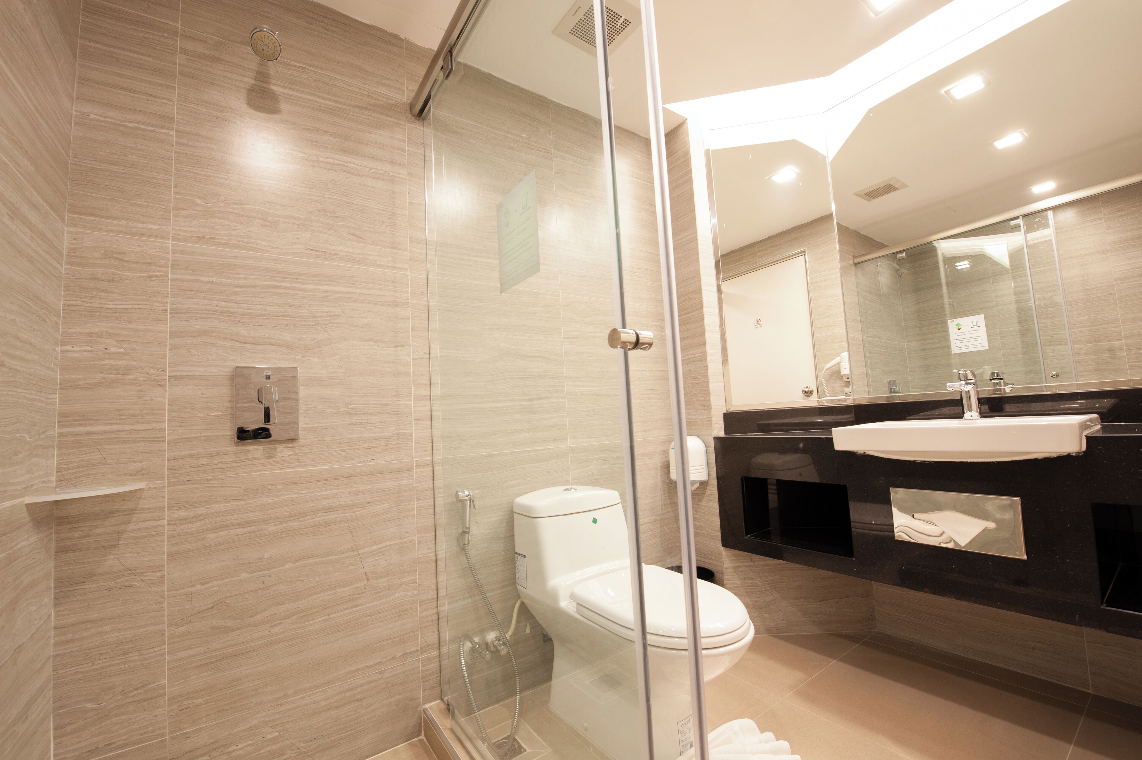 A modern bathroom with a glass-enclosed shower, a white toilet, and a black vanity with a mirror.