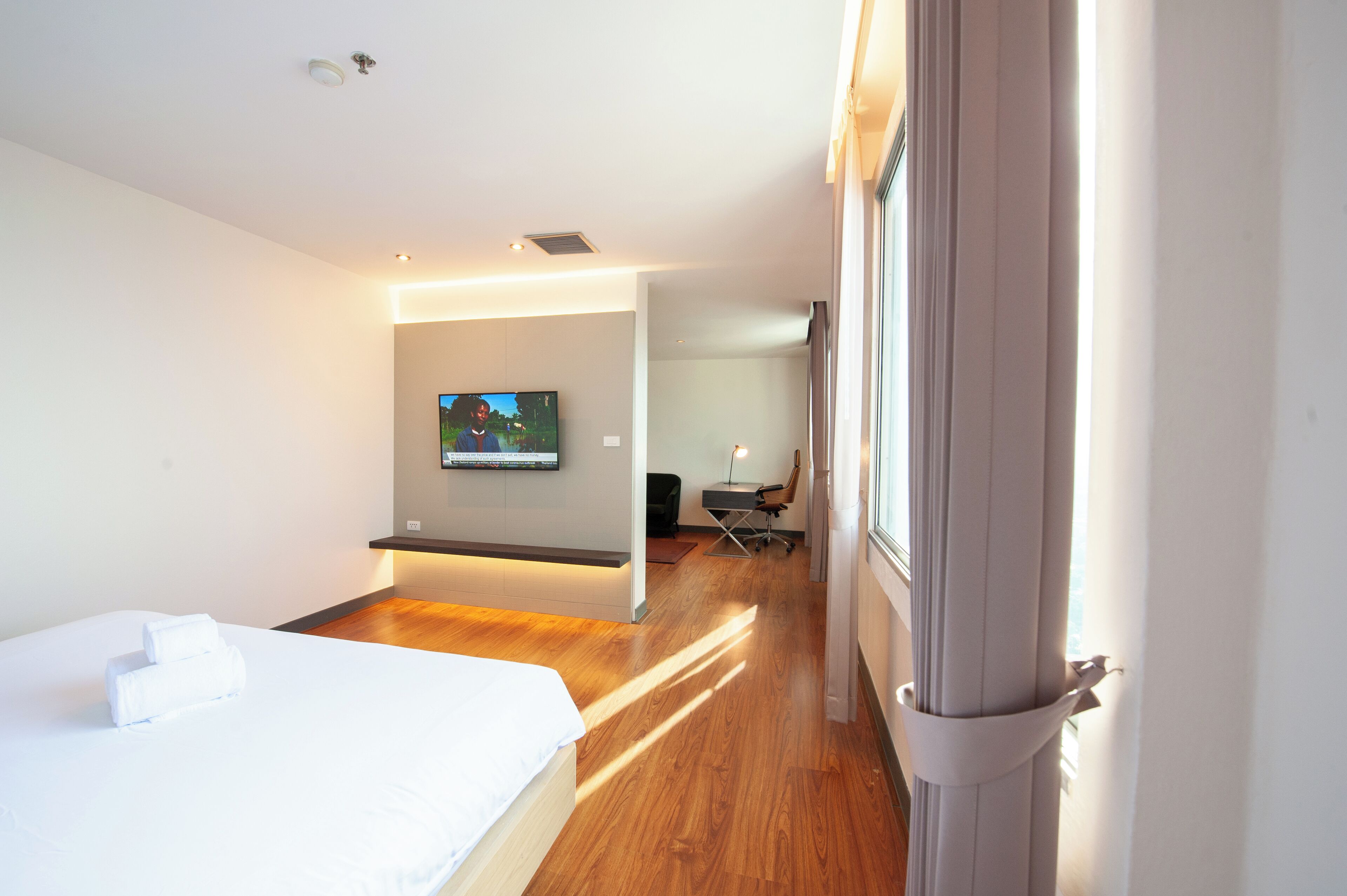 A modern hotel room with a large bed, a flat-screen TV mounted on the wall, and a desk with a chair.
