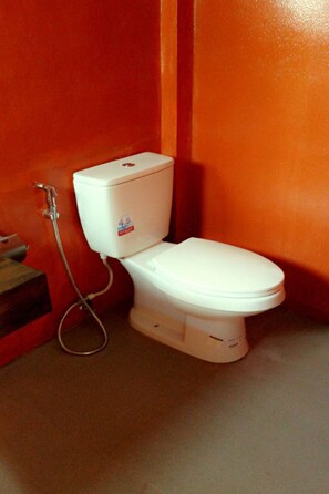 A white toilet with a 4.6 rating sticker, a shower hose, and a red wall. - Cha-am Eco Camp (Cha-am)