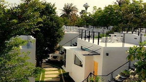 A modern hotel with a central staircase, surrounded by lush greenery and white buildings. - Cha-am Eco Camp (Cha-am)