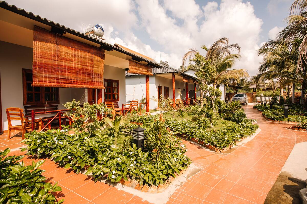 A traditional-style building with a tiled patio, outdoor seating, and lush greenery.