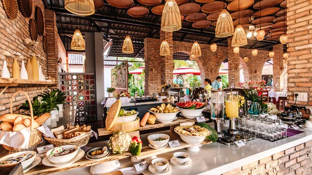 Ein reichhaltiges Buffet mit verschiedenen Speisen und einer Getränkestation, präsentiert in einem Raum mit Backsteinwänden und hängenden Korbstühlen.