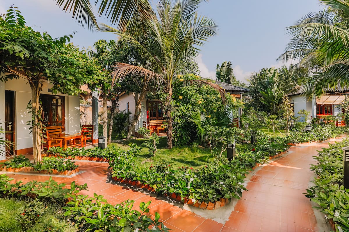 A tropical garden with a paved walkway, wooden furniture, and lush greenery.