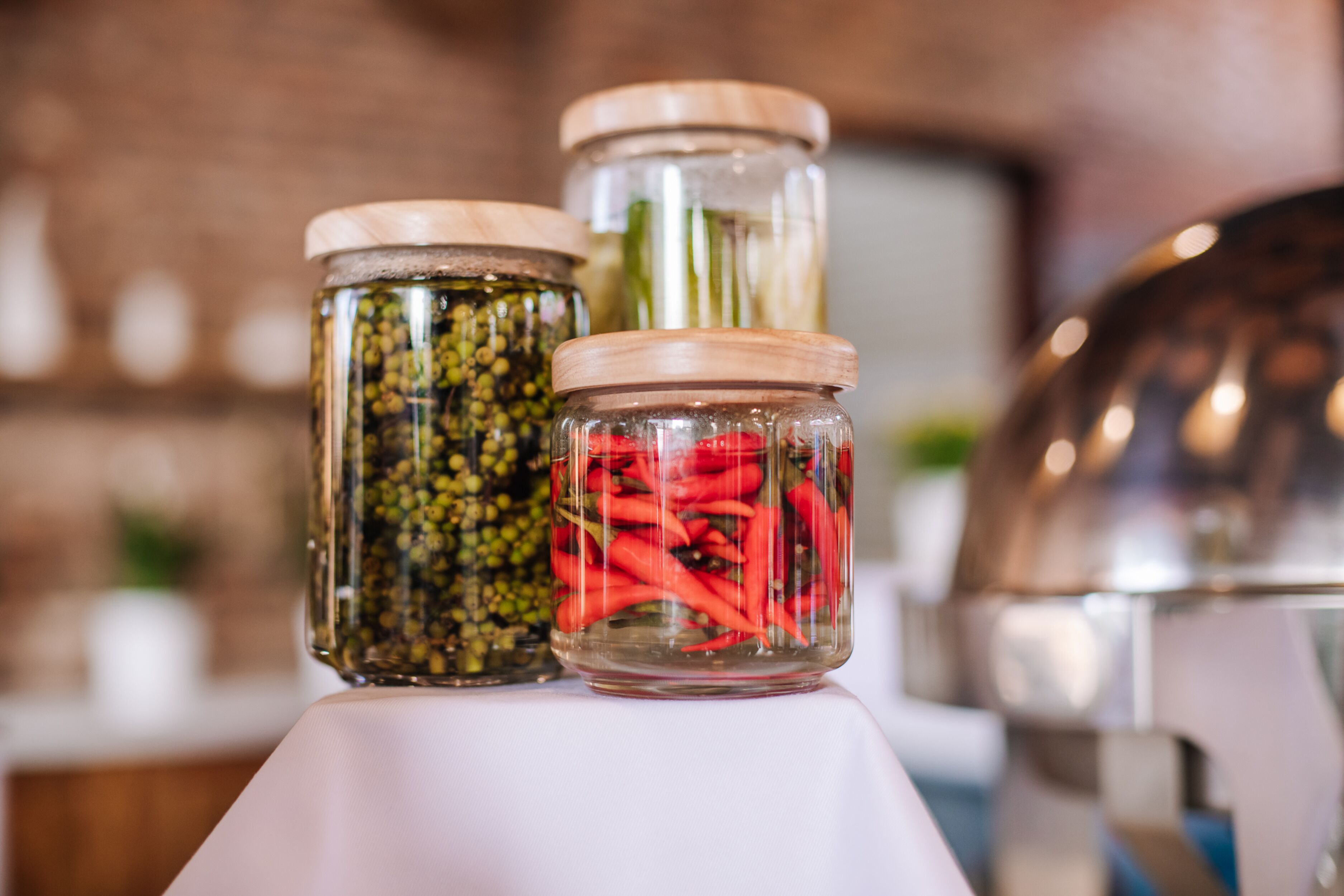 Three glass jars with wooden lids containing various preserved foods.