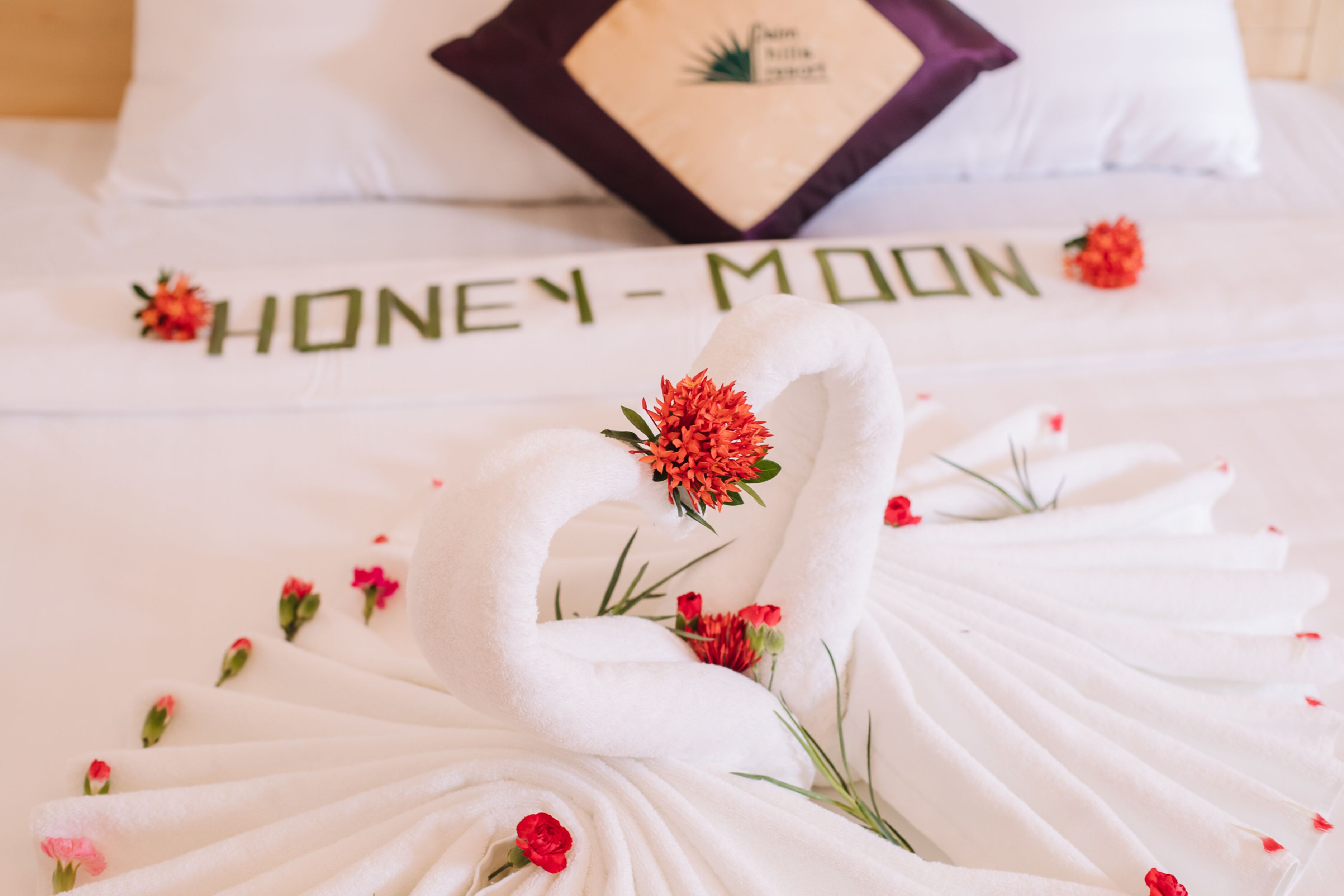 A bed with a swan towel arrangement and the text "HONEY-MOON" on the pillow.
