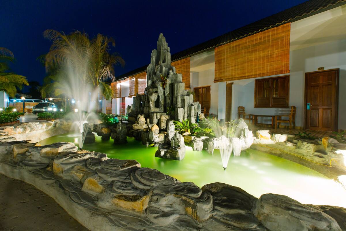 A nighttime view of a hotel with a landscaped garden featuring a rock formation and a fountain.