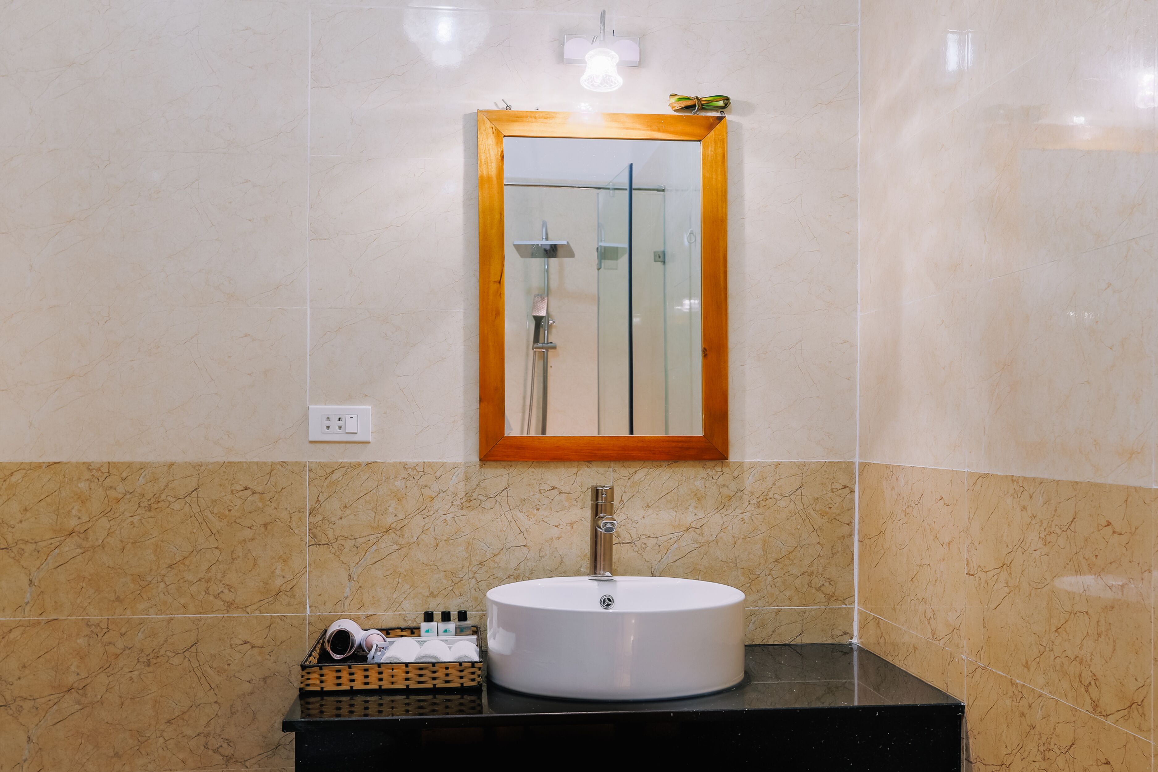 A bathroom with a round sink, a mirror with a wooden frame, and a shower visible in the mirror reflection.