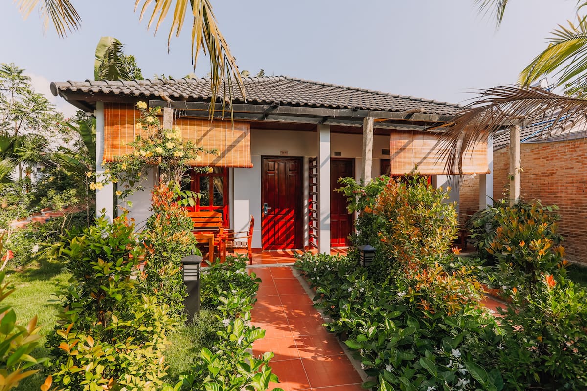 A house with a tiled roof, a red door, and a garden with various plants and a pathway.