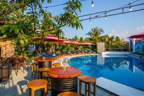 A poolside area with lounge chairs, red umbrellas, and wooden tables.