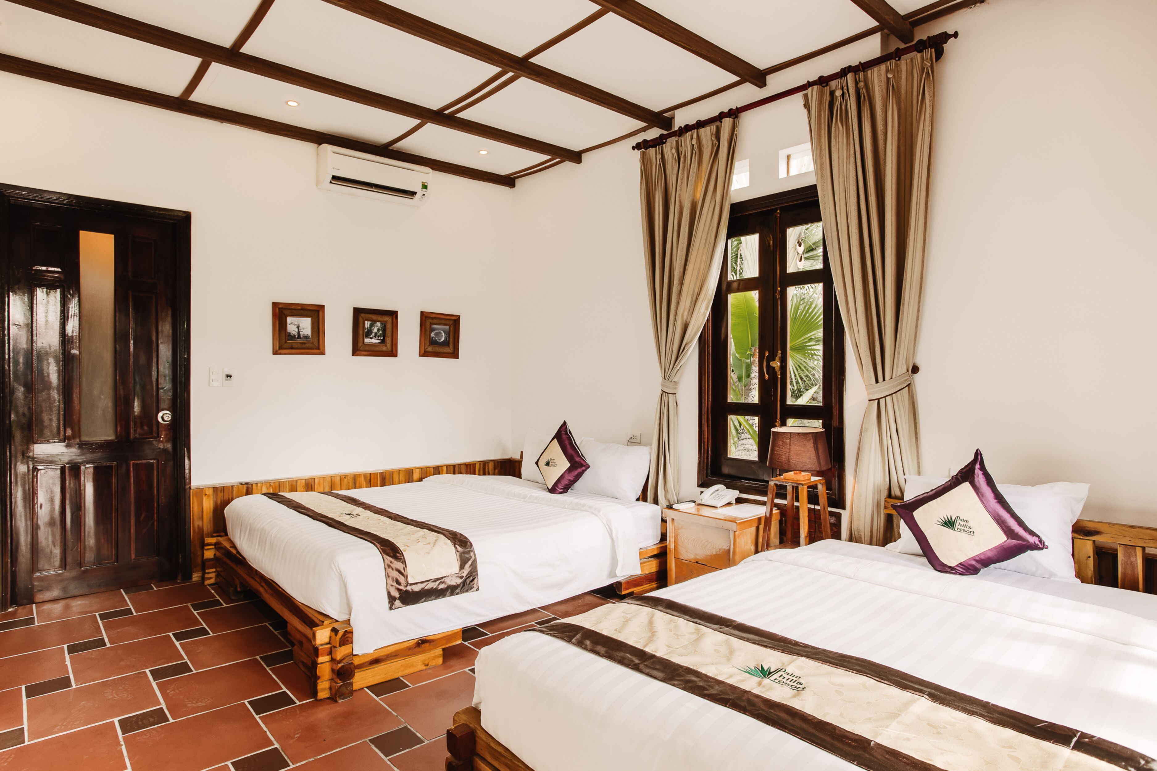Habitación de hotel con dos camas, piso de madera, ventana con cortinas y una puerta.