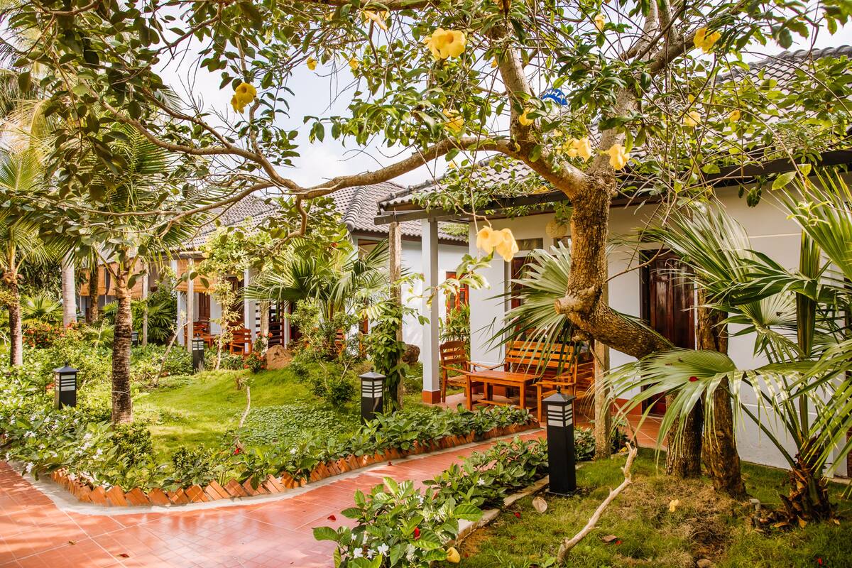 A courtyard with a pathway, a wooden bench, and a white building with a tiled roof.
