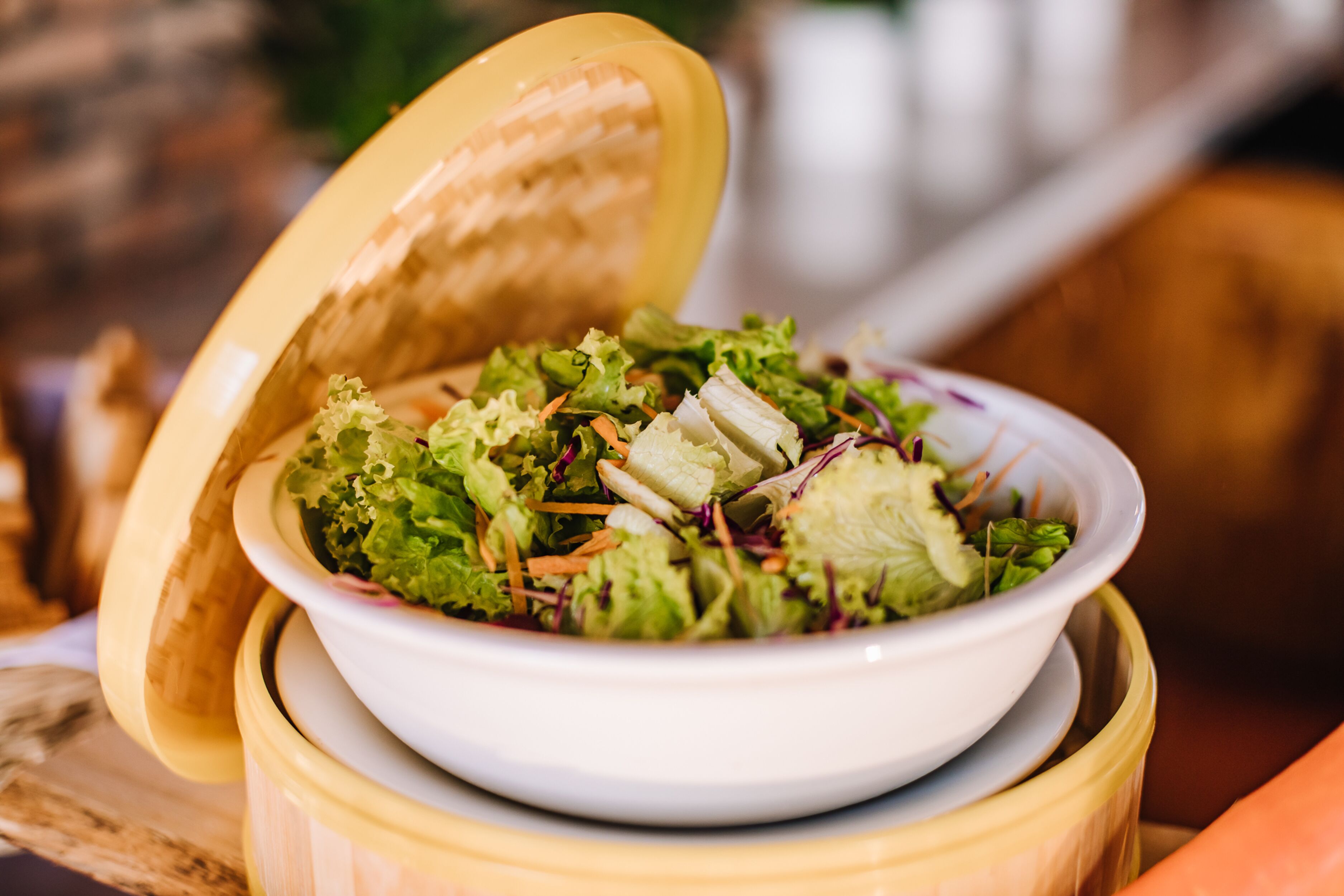 Un bol de ensalada con una tapa sobre un soporte de madera.