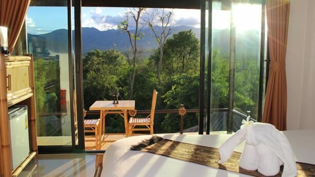 Un dormitorio con un ventanal que ofrece vistas a la montaña. Hay una cama, una mesa de madera y una silla.