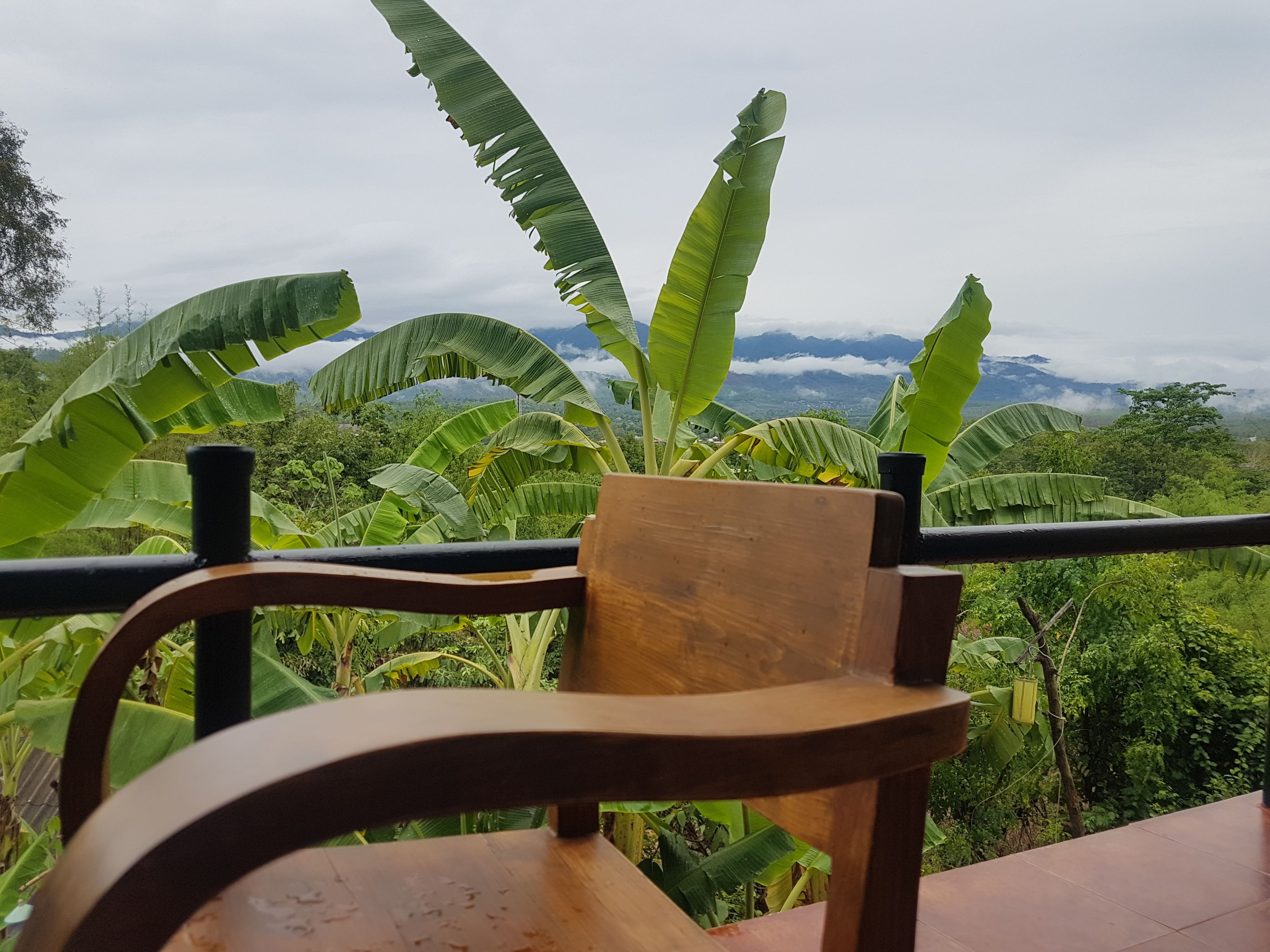 A wooden chair with a view of lush greenery and mountains in the background.