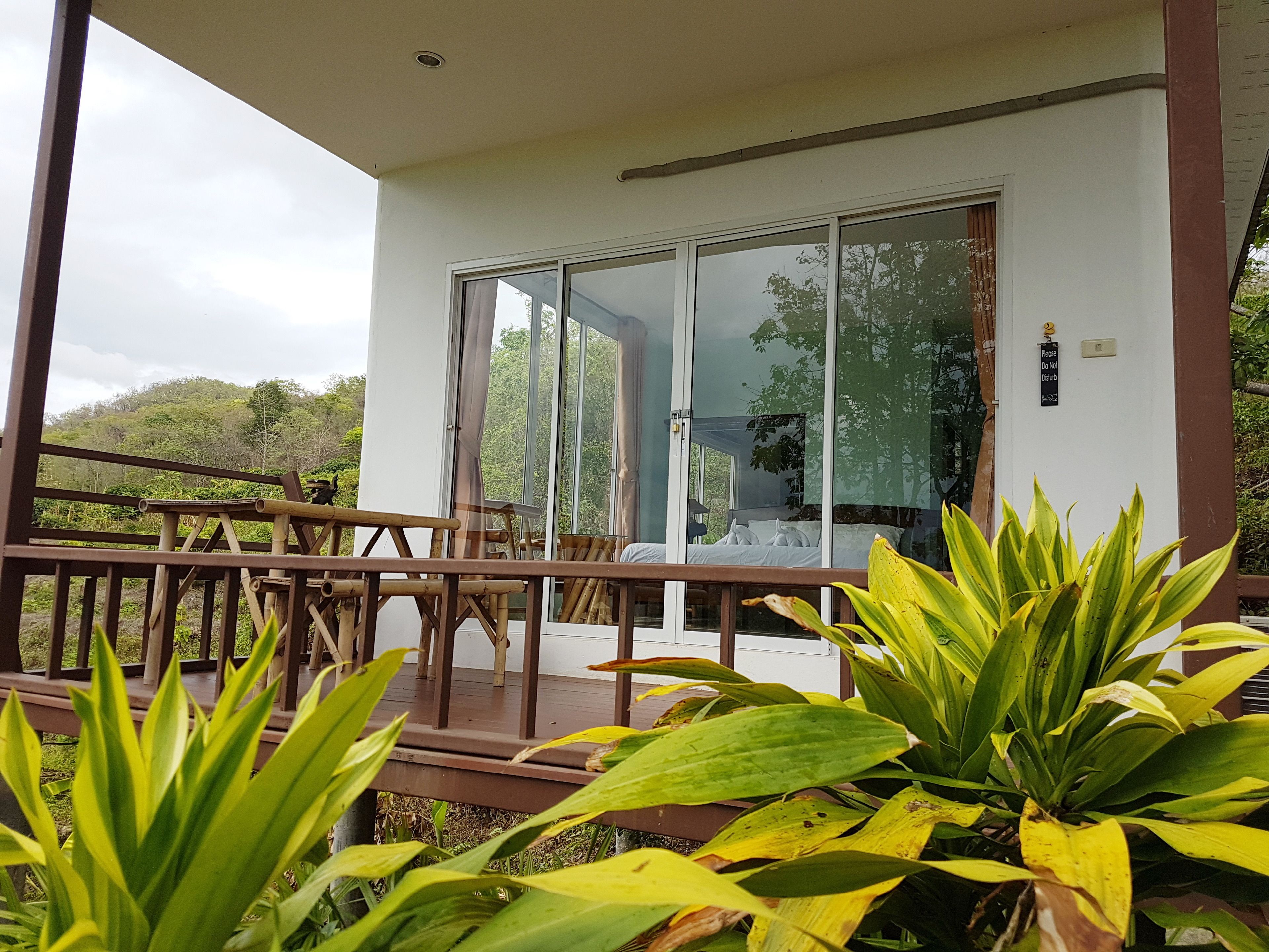 A hotel room with a sliding glass door, a wooden deck, and lush greenery.