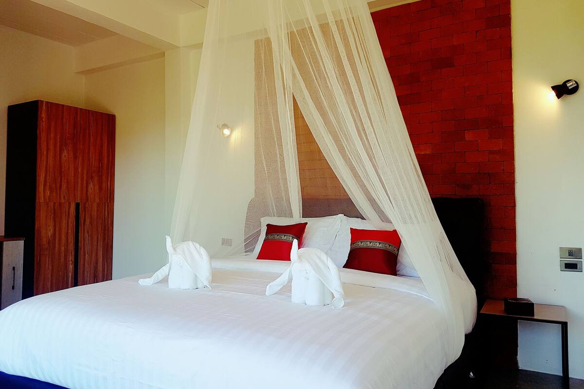 A bed with white bedding and red pillows, a wooden wardrobe, and a red brick wall.