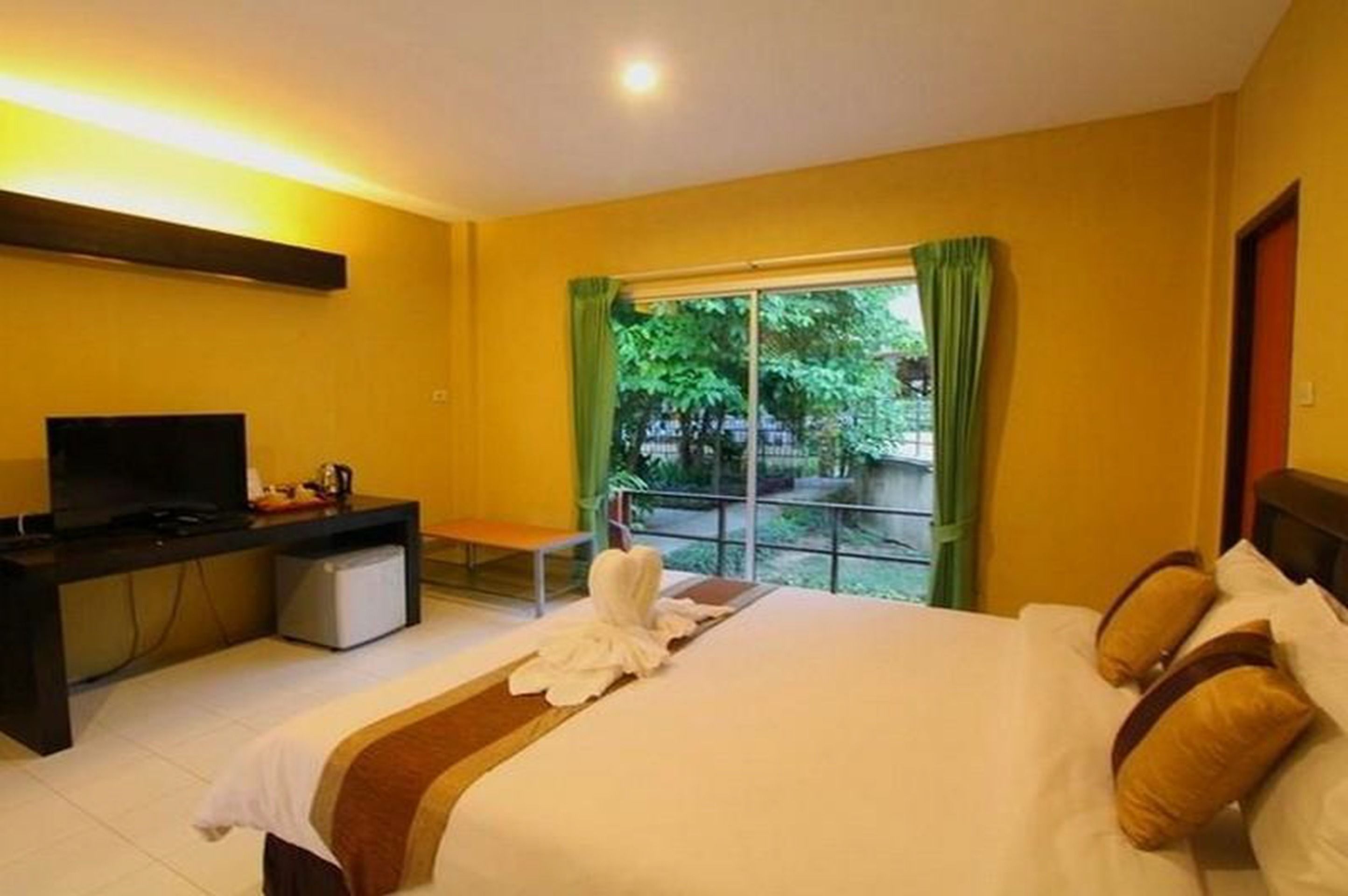 Une chambre d’hôtel avec un lit, un bureau avec une télévision et une fenêtre avec des rideaux.