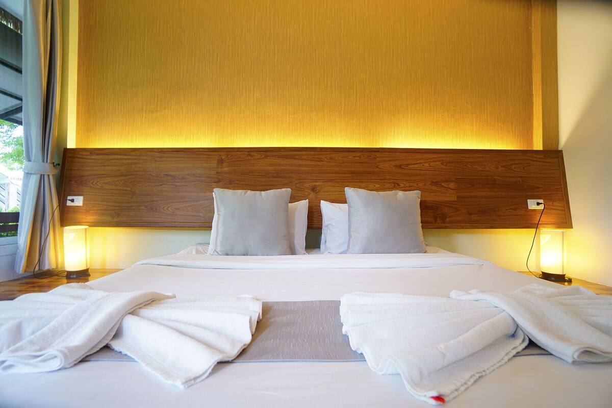 Een hotelkamer met een houten hoofdeinde, witte beddengoed en twee bedlampjes.