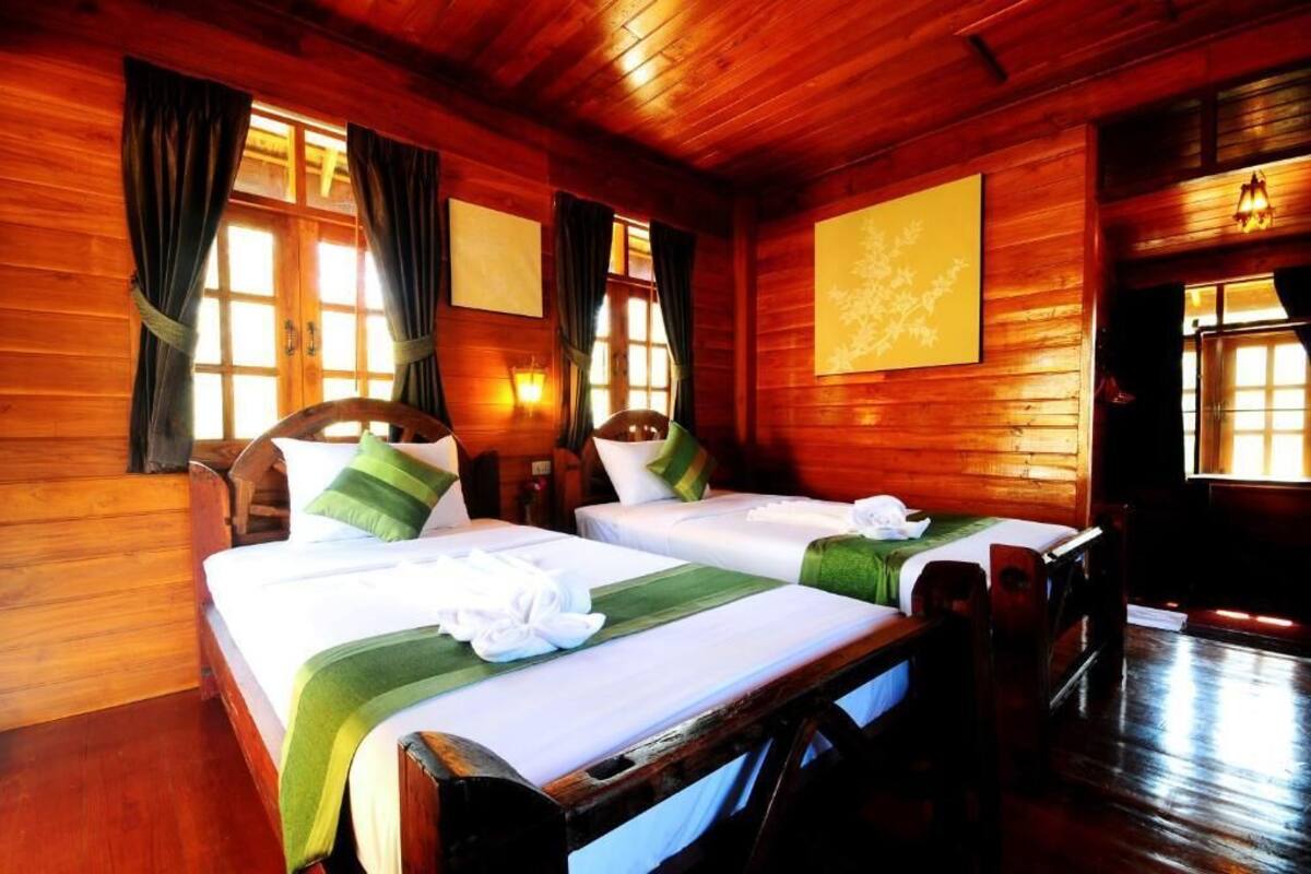 Een houten kamer in blokhutstijl met twee bedden, elk met groen en wit beddengoed, en een houten hoofdbord.