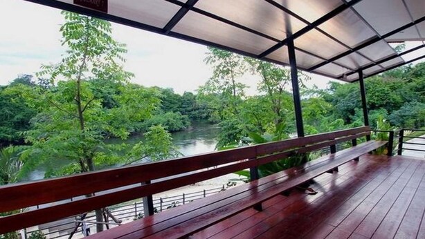 Een houten terras met een bankje, met uitzicht op een rivier omringd door weelderige begroeiing.