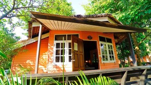 Een houten huis met twee verdiepingen en een veranda, omgeven door weelderige begroeiing.
