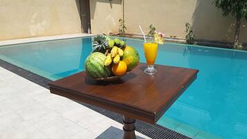 A poolside table with a fruit basket and a glass of orange juice.