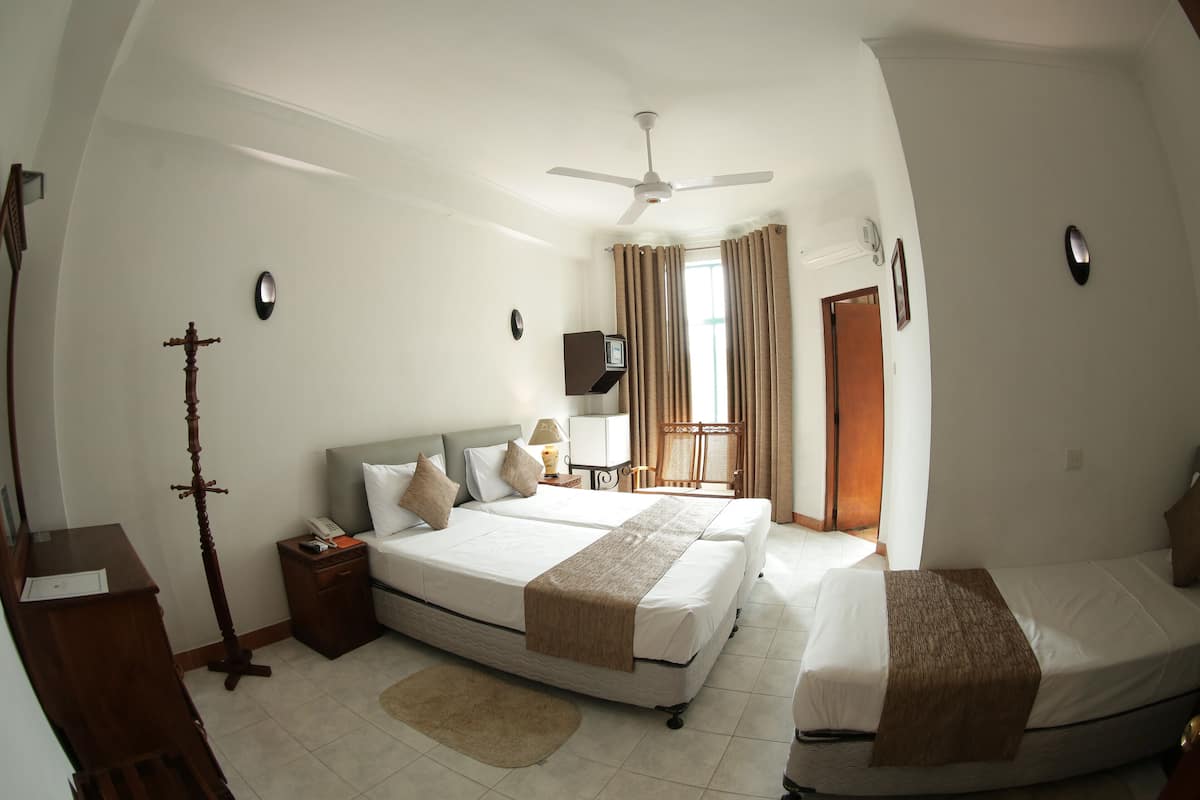 A hotel room with two beds, a ceiling fan, a desk, a lamp, and a window with curtains.