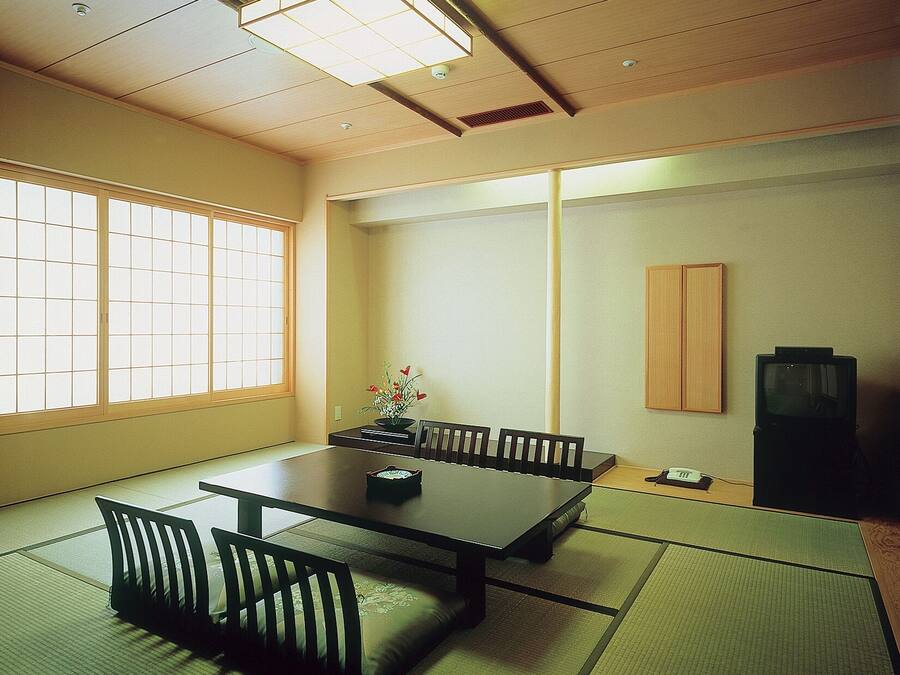 Ein traditioneller japanischer Raum mit Tatami-Boden, einem niedrigen Tisch mit Kissen, einer kleinen Holzkabine und einem Fernseher.
